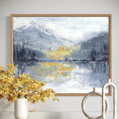 Framed abstract landscape painting with mountains and water, placed on a wall above a vase with yellow flowers.