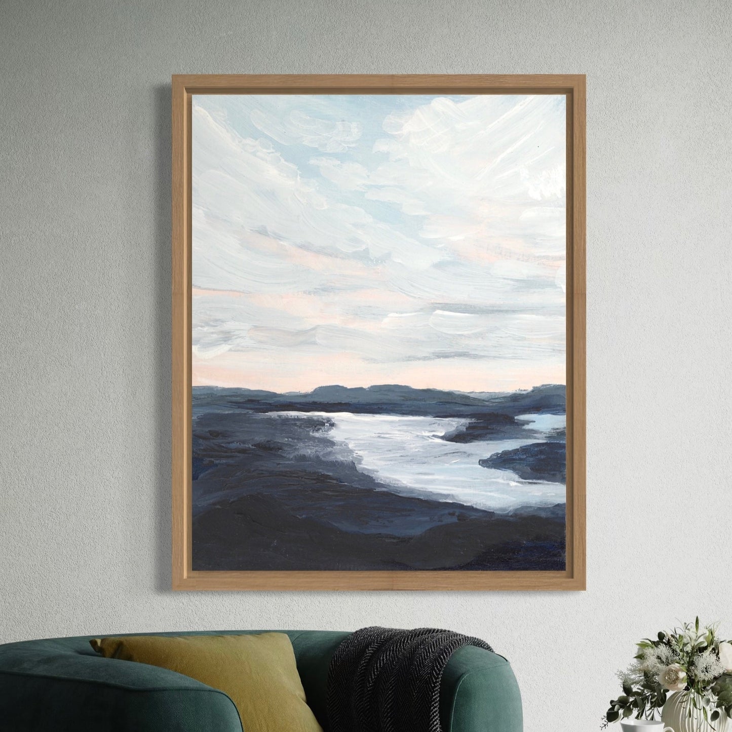 Framed artwork of a landscape with water and sky on a wall above a green sofa.