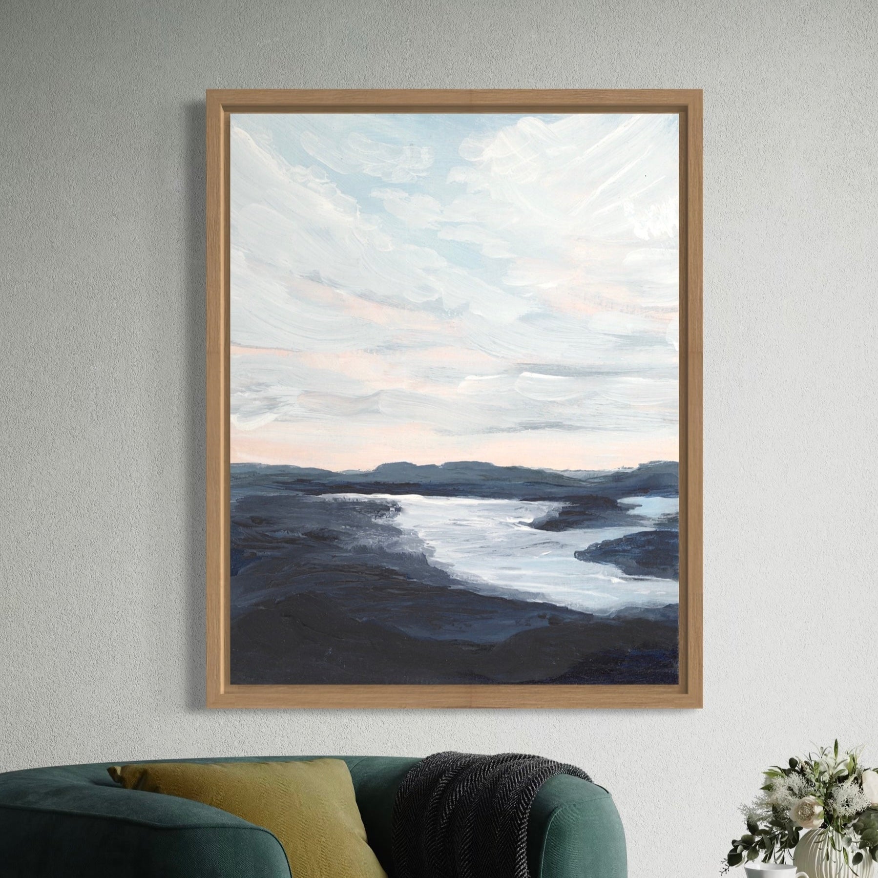 Framed artwork of a landscape with water and sky on a wall above a green sofa.