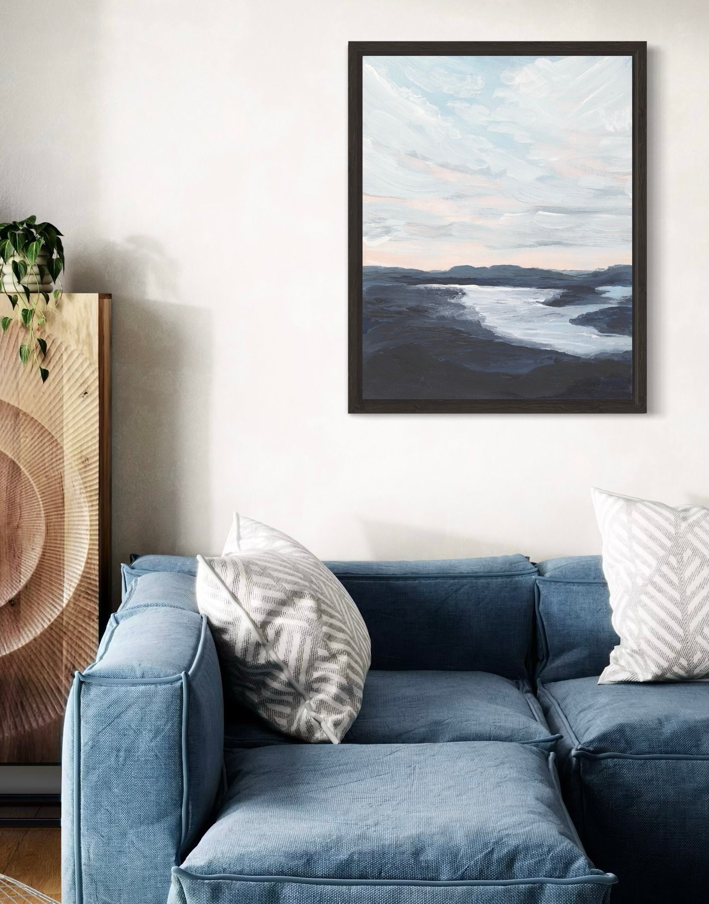 Blue sofa with decorative pillows in a living room setting, featuring a framed landscape painting on the wall.