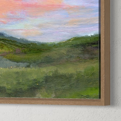 Framed painting of a landscape with a colorful sky on a white wall