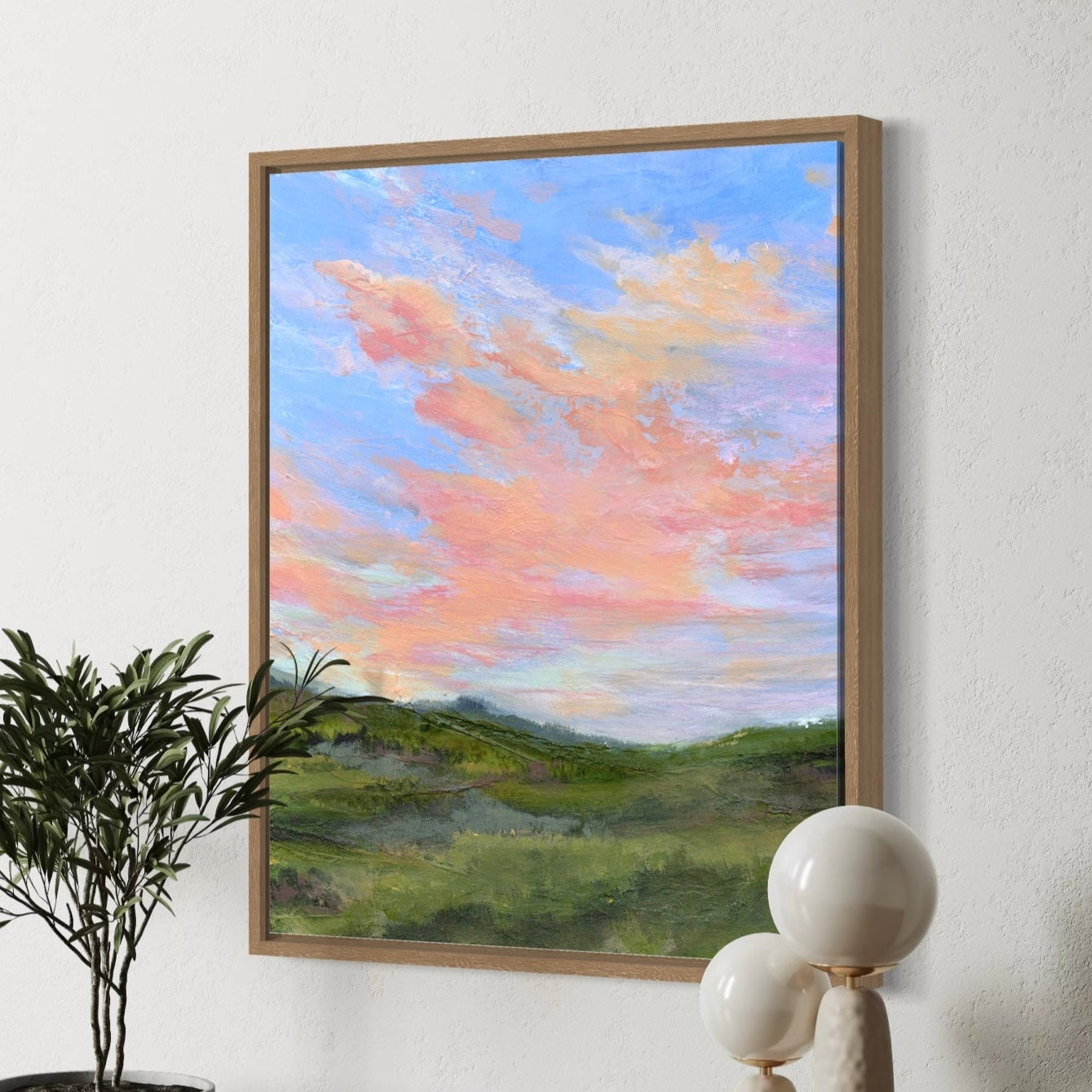Framed artwork of a landscape with a plant and sculpture on a wooden bench.