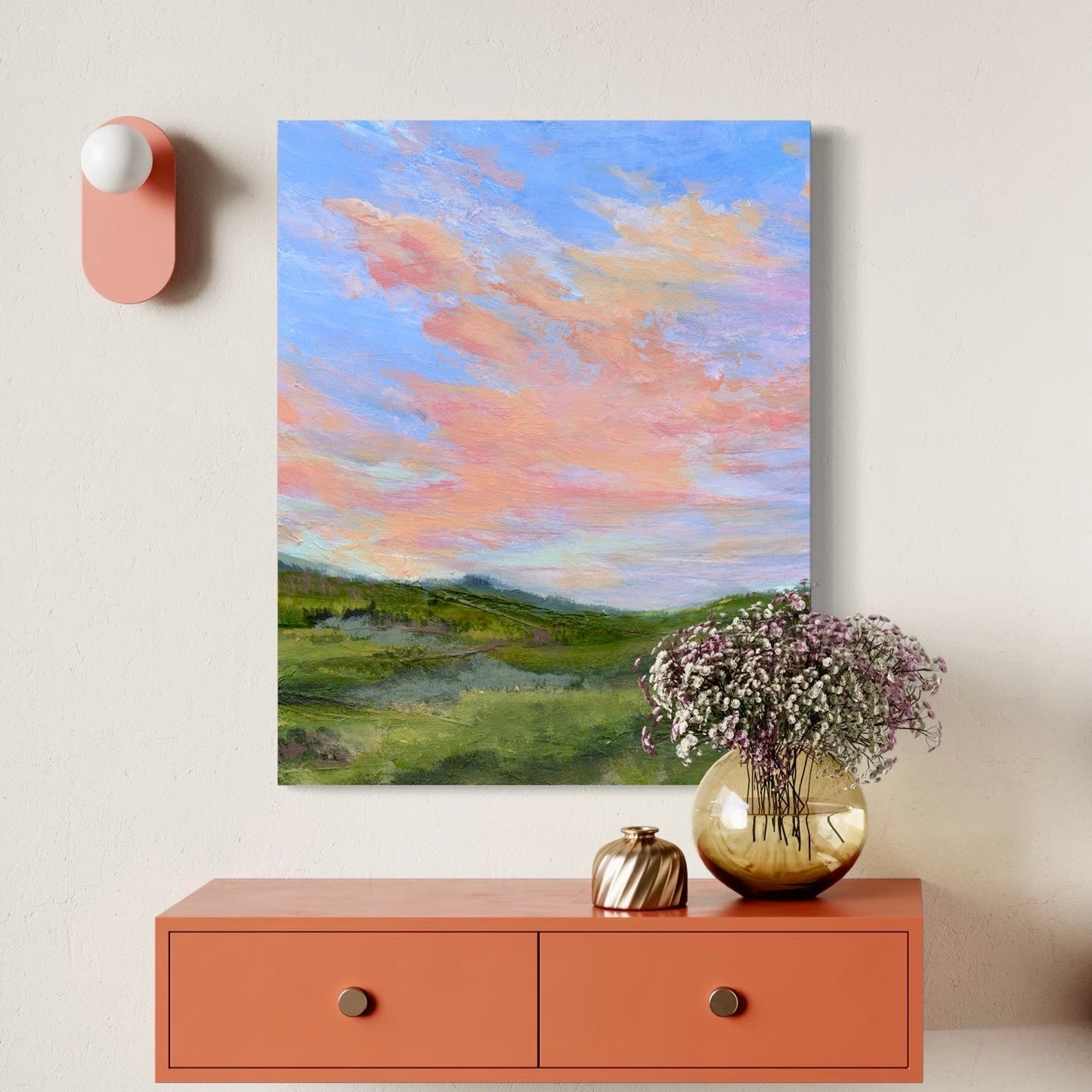 Framed artwork of a landscape with a pink wall-mounted device and a vase with flowers on a shelf.