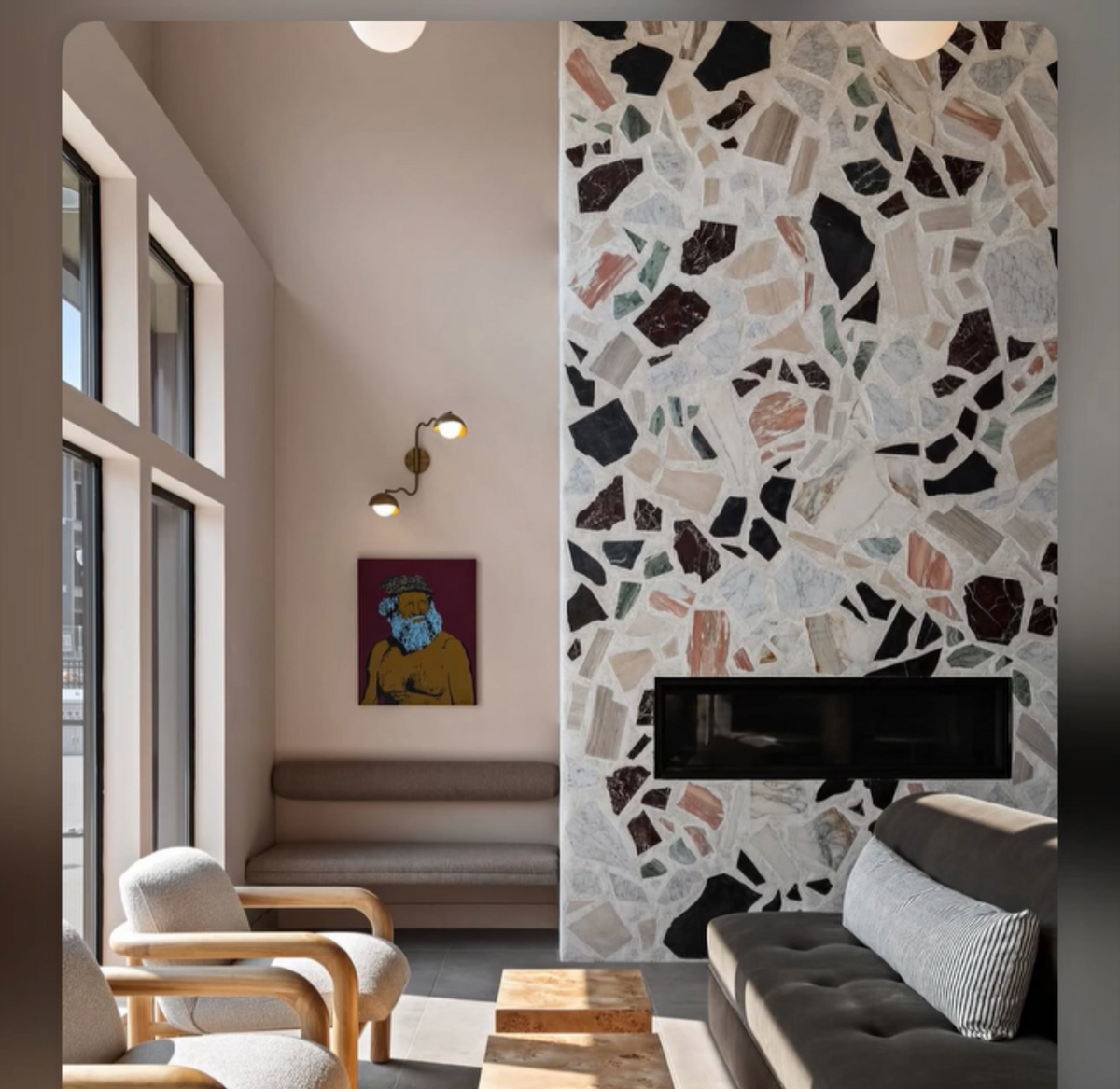a modern living room interior with a fireplace, terrazzo wall, wooden chairs, and a dark sofa.