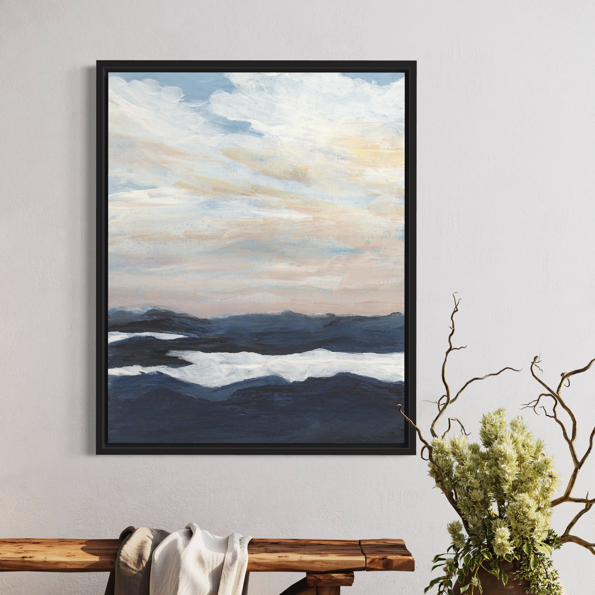 Framed landscape painting of mountains and clouds on a wall above a wooden bench.