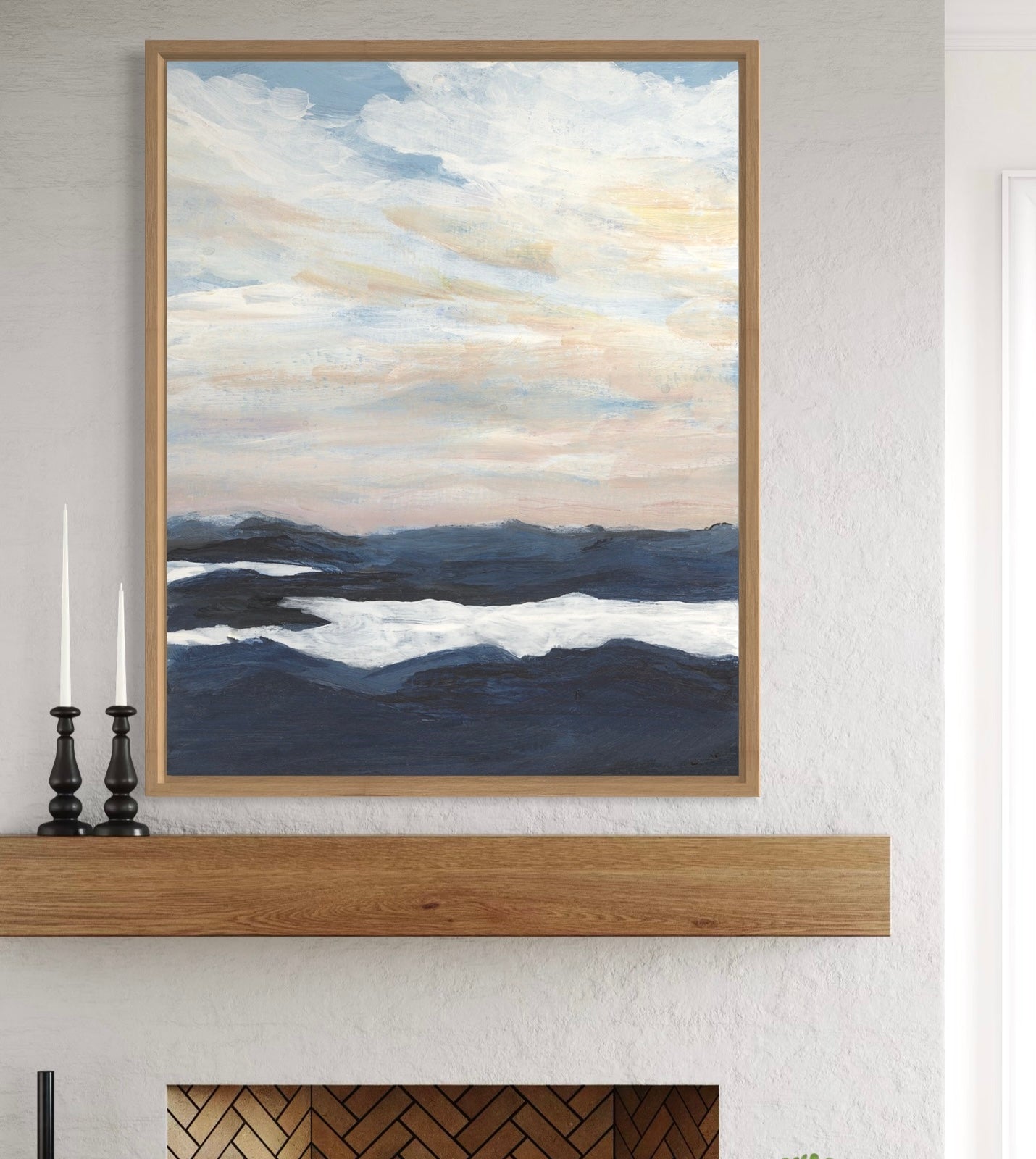 Framed artwork of a landscape with mountains and clouds on a wall above a fireplace.
