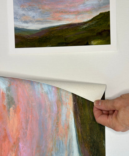 Person peeling back a protective layer on a framed landscape painting.