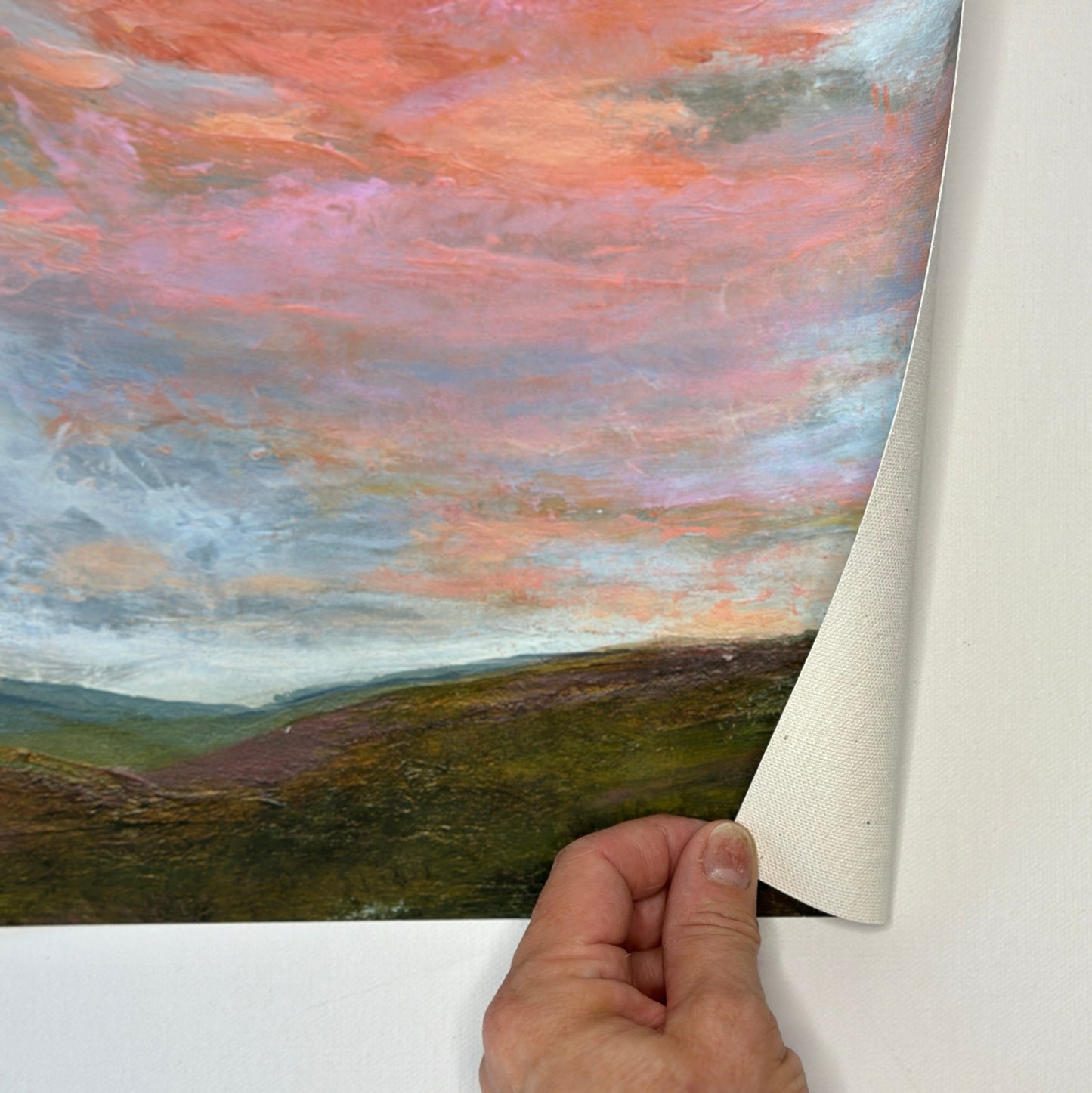 Hand peeling back a piece of paper to reveal a landscape painting with a colorful sky.
