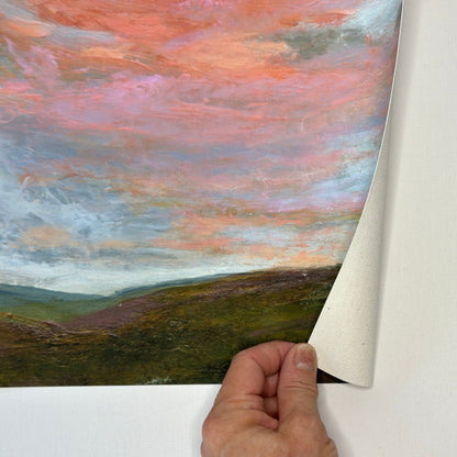 Hand peeling back a piece of paper to reveal a landscape painting with a colorful sky.