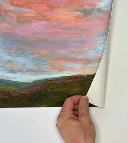 Hand peeling back a piece of paper to reveal a landscape painting with a colorful sky.