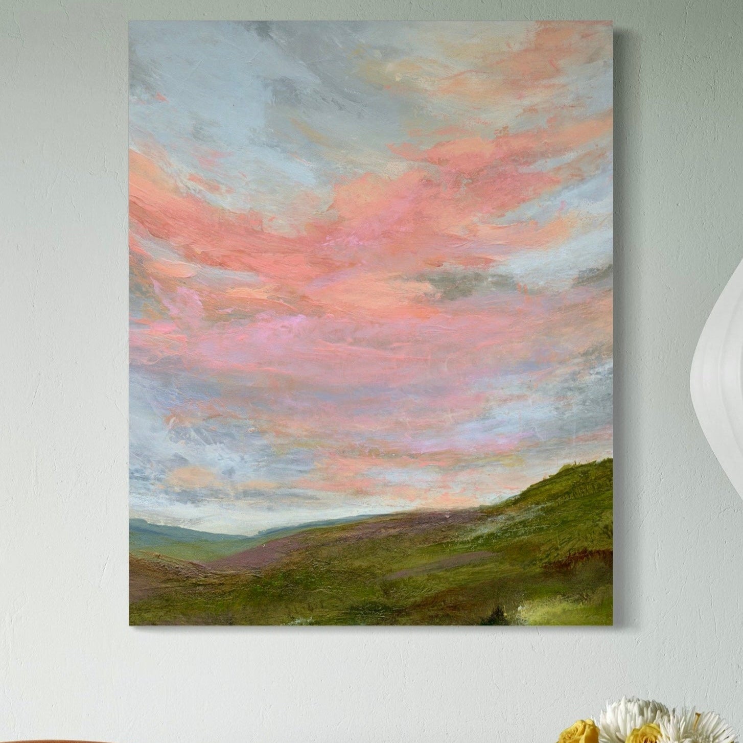 Painting of a landscape with a pink sky on a wall above a brown chair.