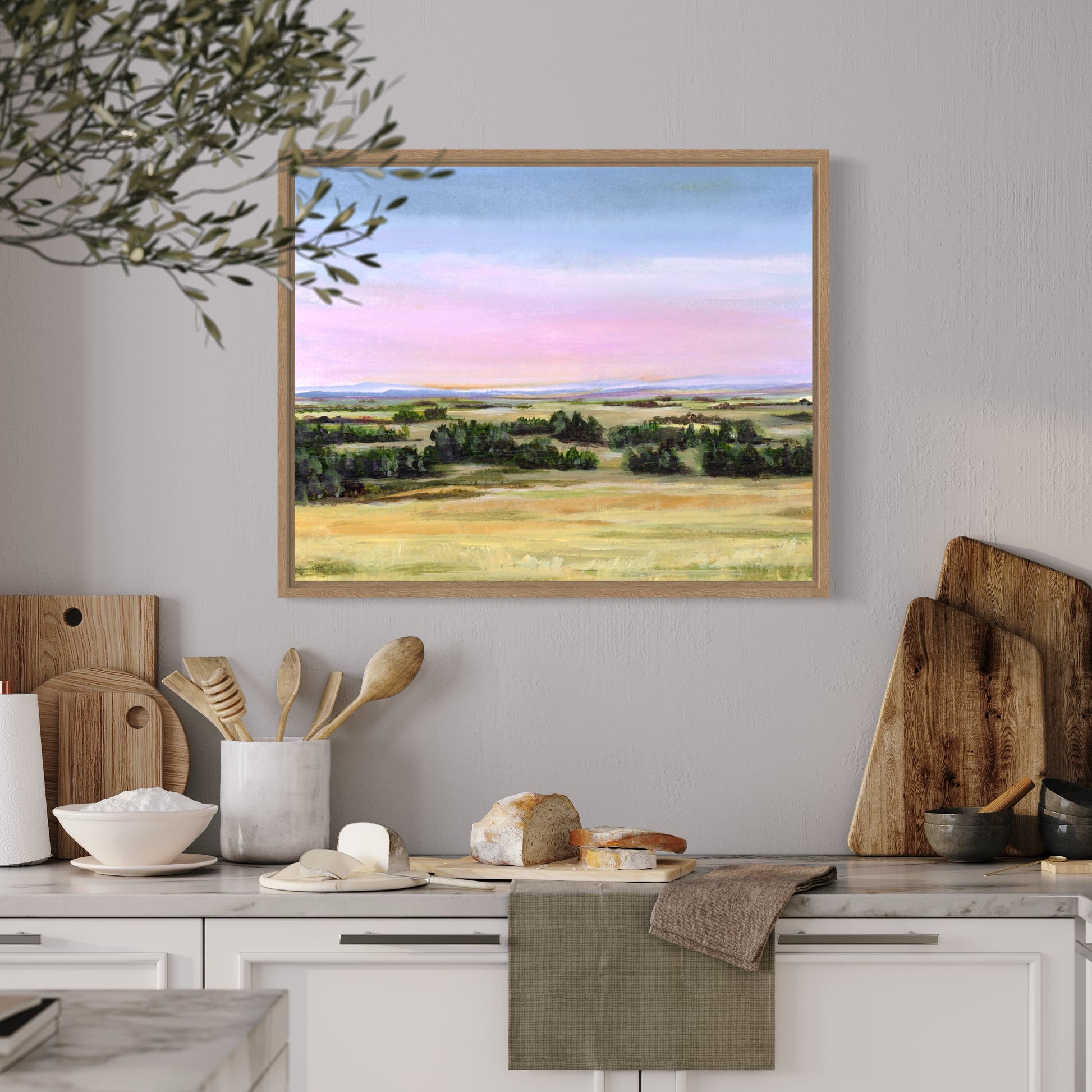 Framed landscape painting above a kitchen counter with wooden cutting boards and utensils.