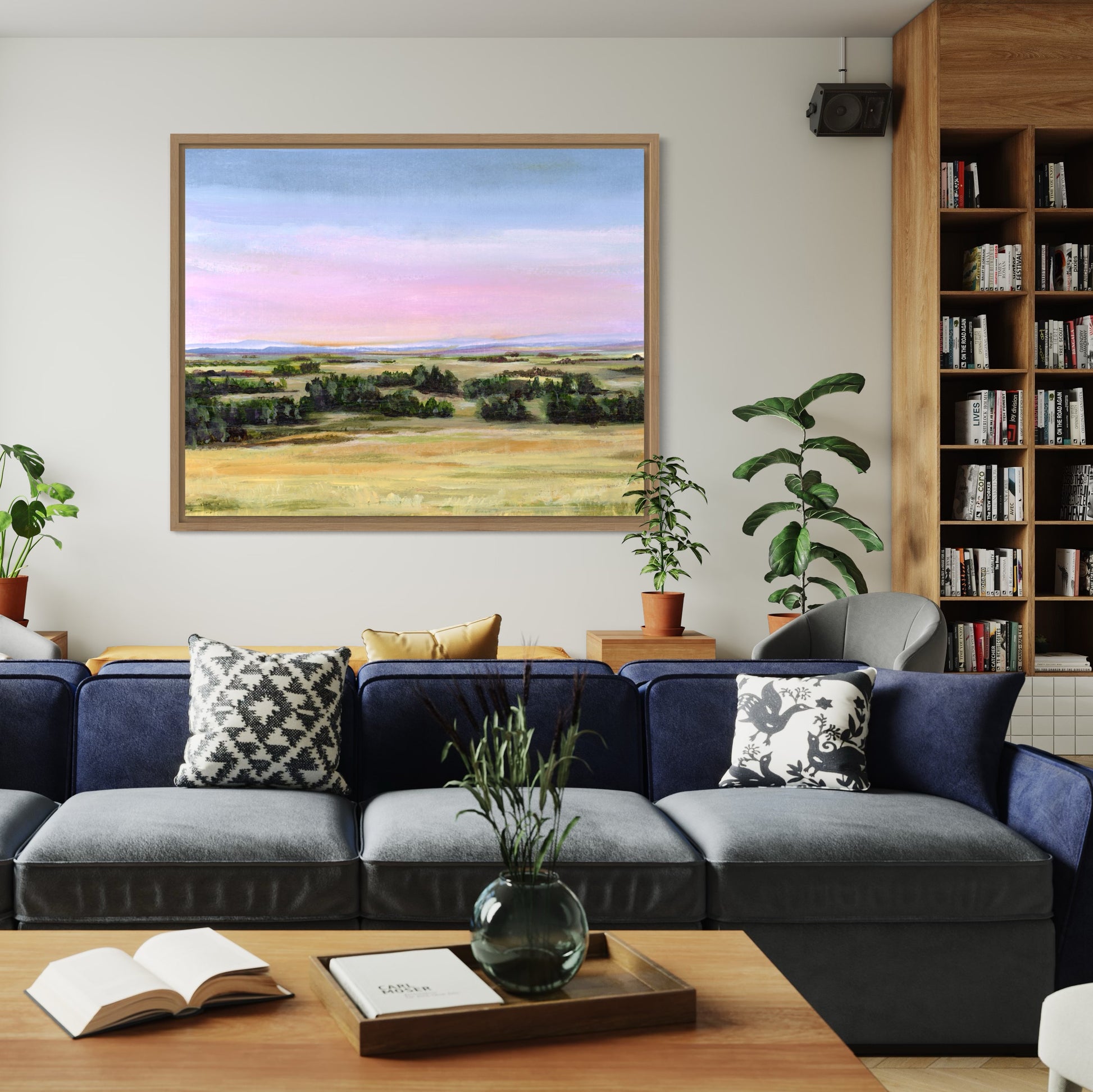 Living room with a blue sofa, framed landscape painting, and bookshelf.