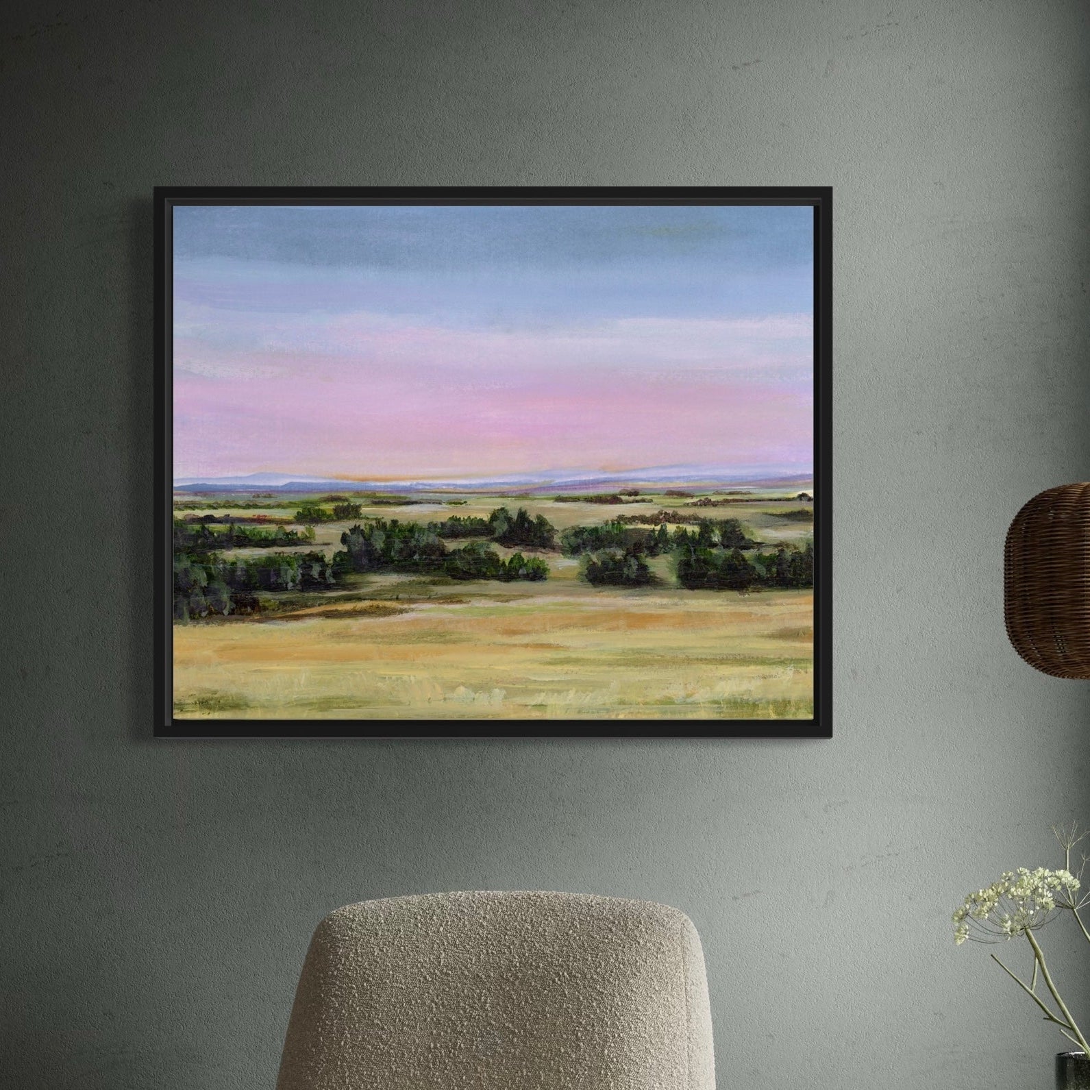 Framed landscape painting on a wall with a chair and plant in the foreground