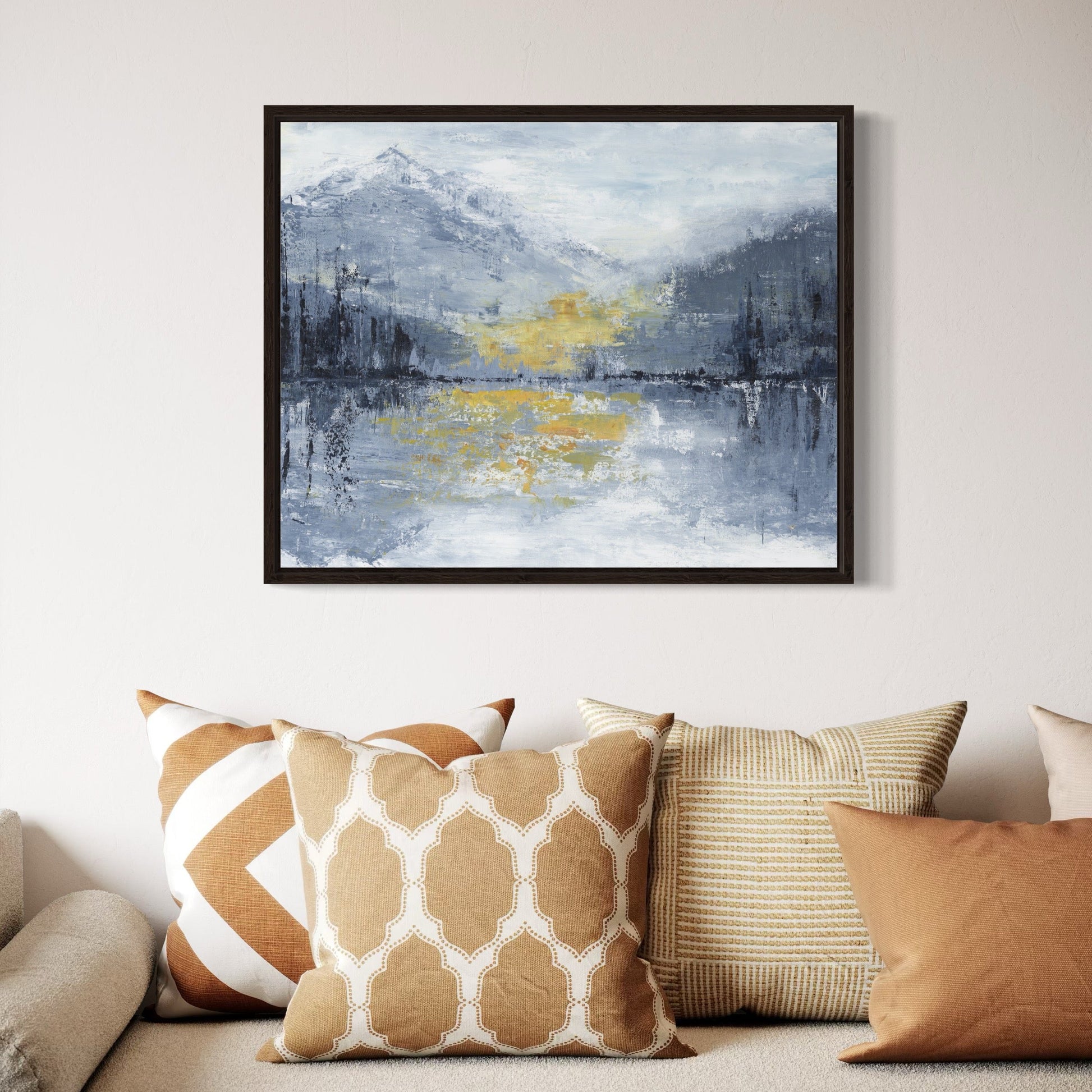 Framed abstract painting on a wall above a sofa with patterned cushions.