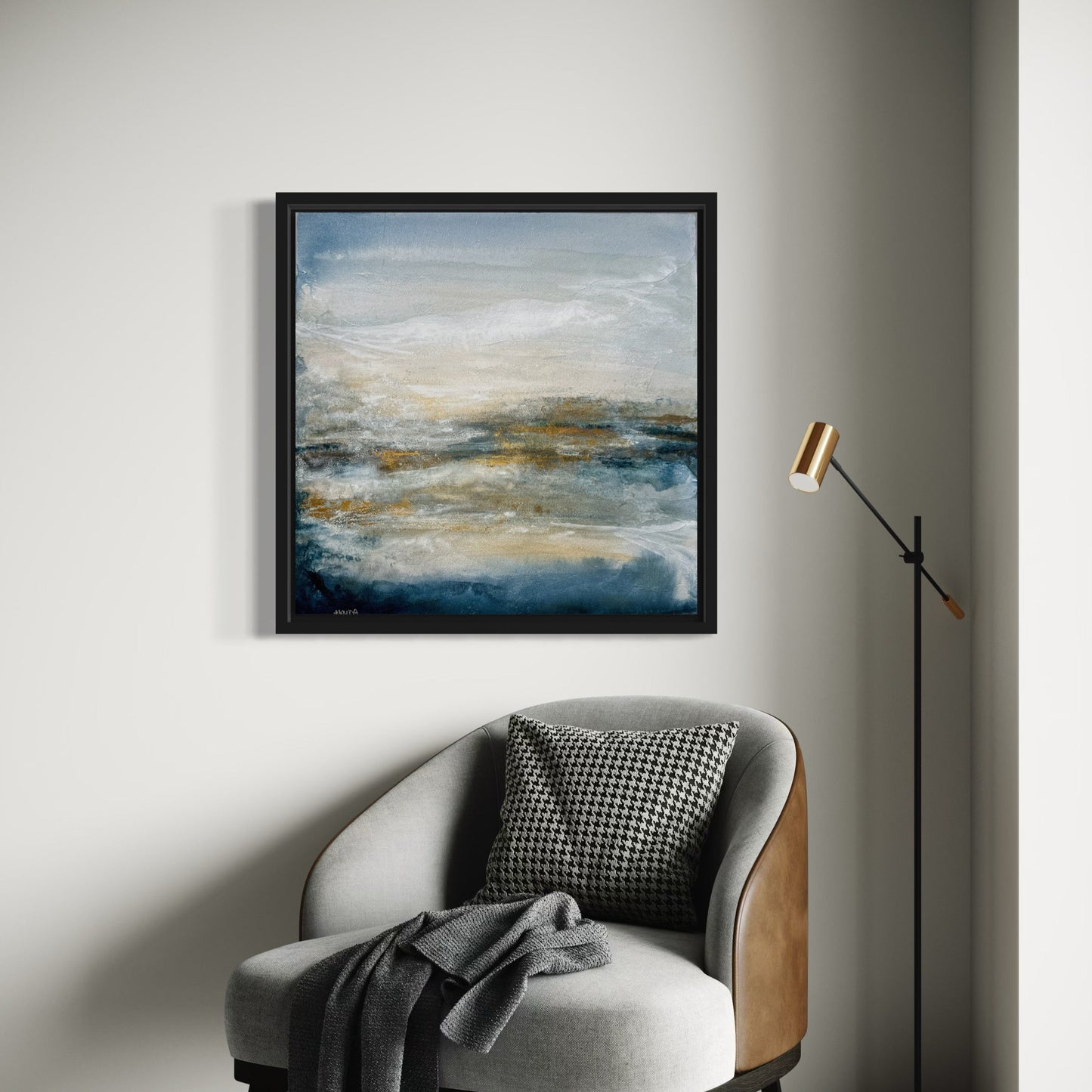 Framed abstract painting on a wall above a chair with a blanket and pillow.