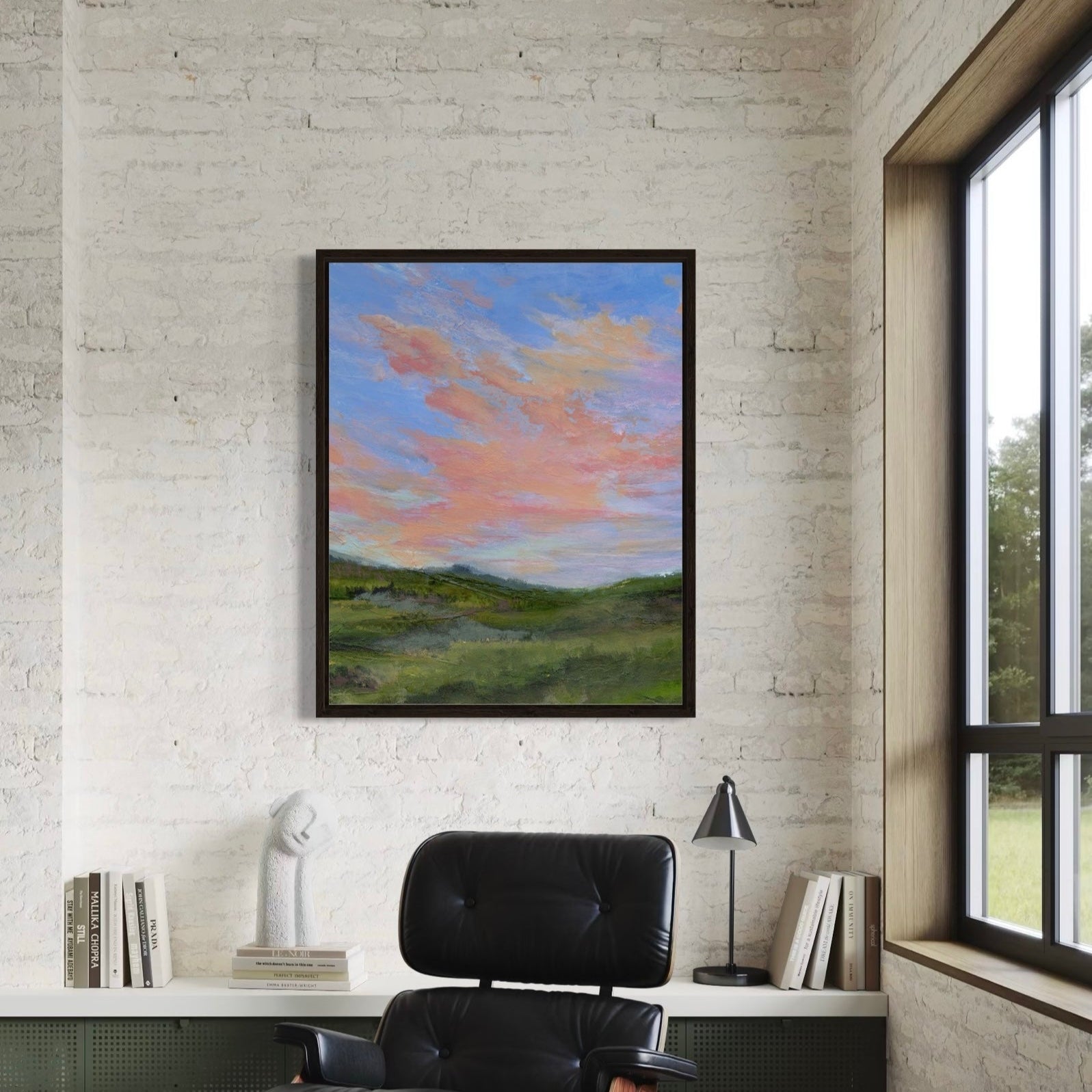 Framed artwork of a landscape with a colorful sky in a room with a brick wall and window.