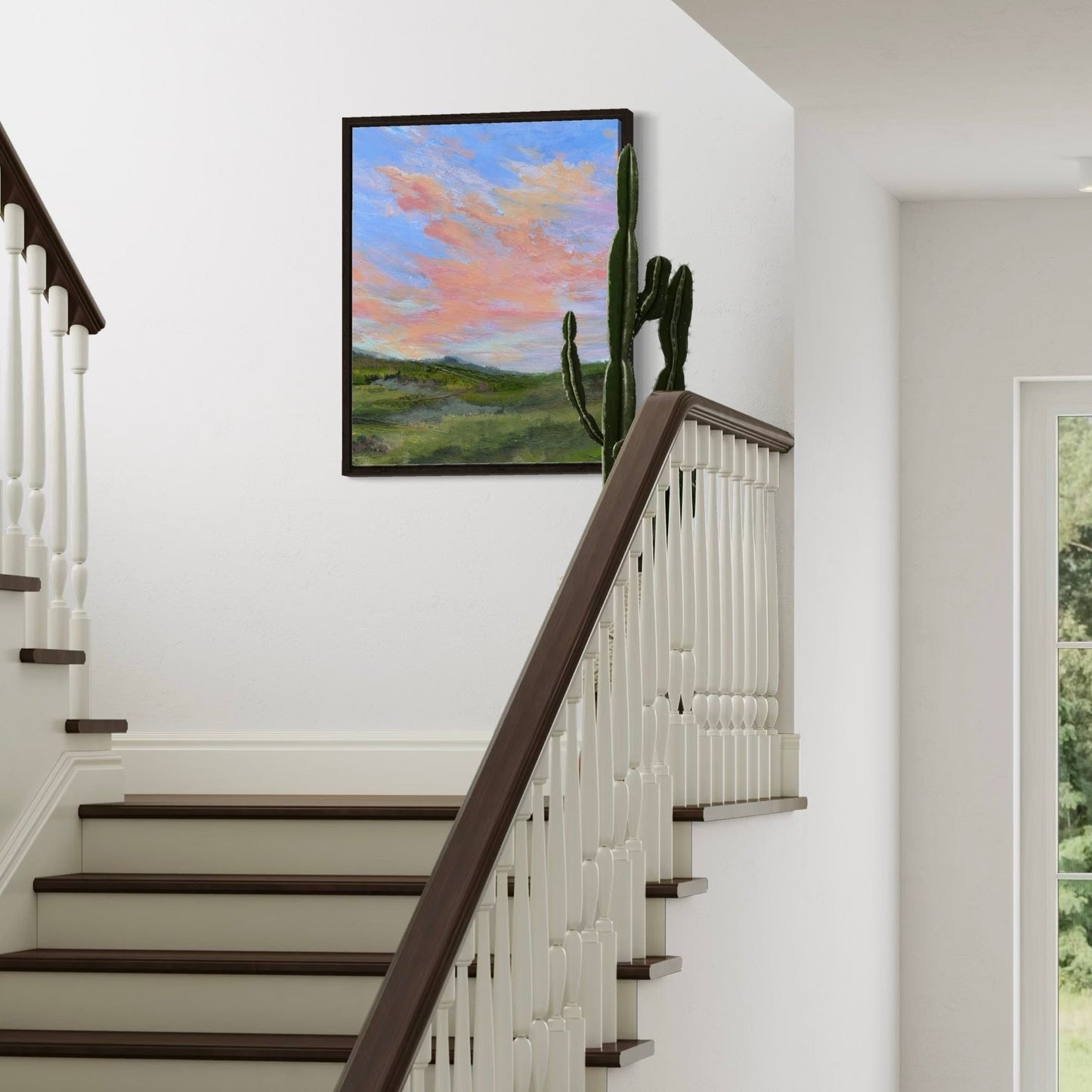 Staircase with wooden handrail and white balusters, featuring a framed painting of a landscape with cacti on the wall.