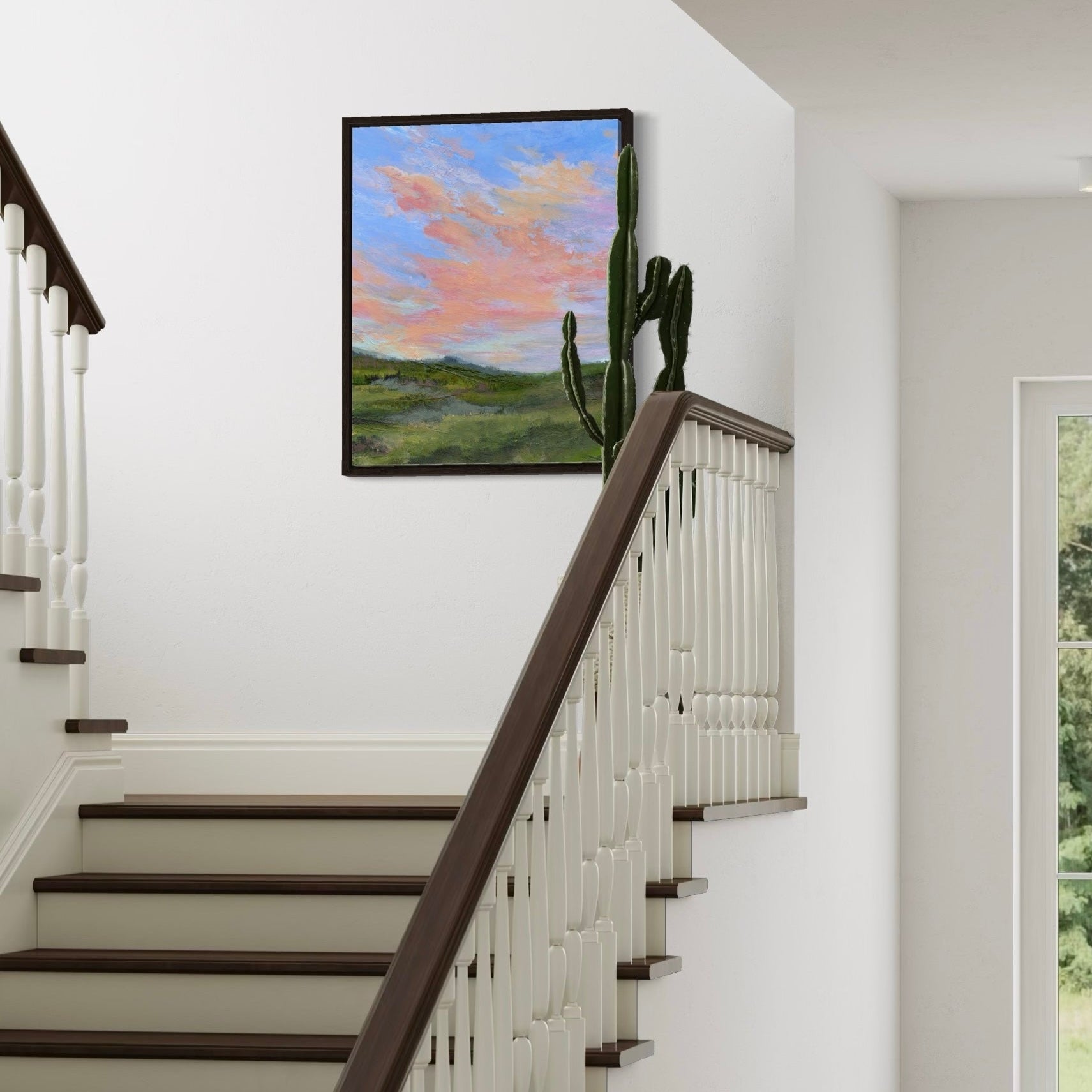 Staircase with wooden handrail and white balusters, featuring a framed painting of a landscape with cacti on the wall.