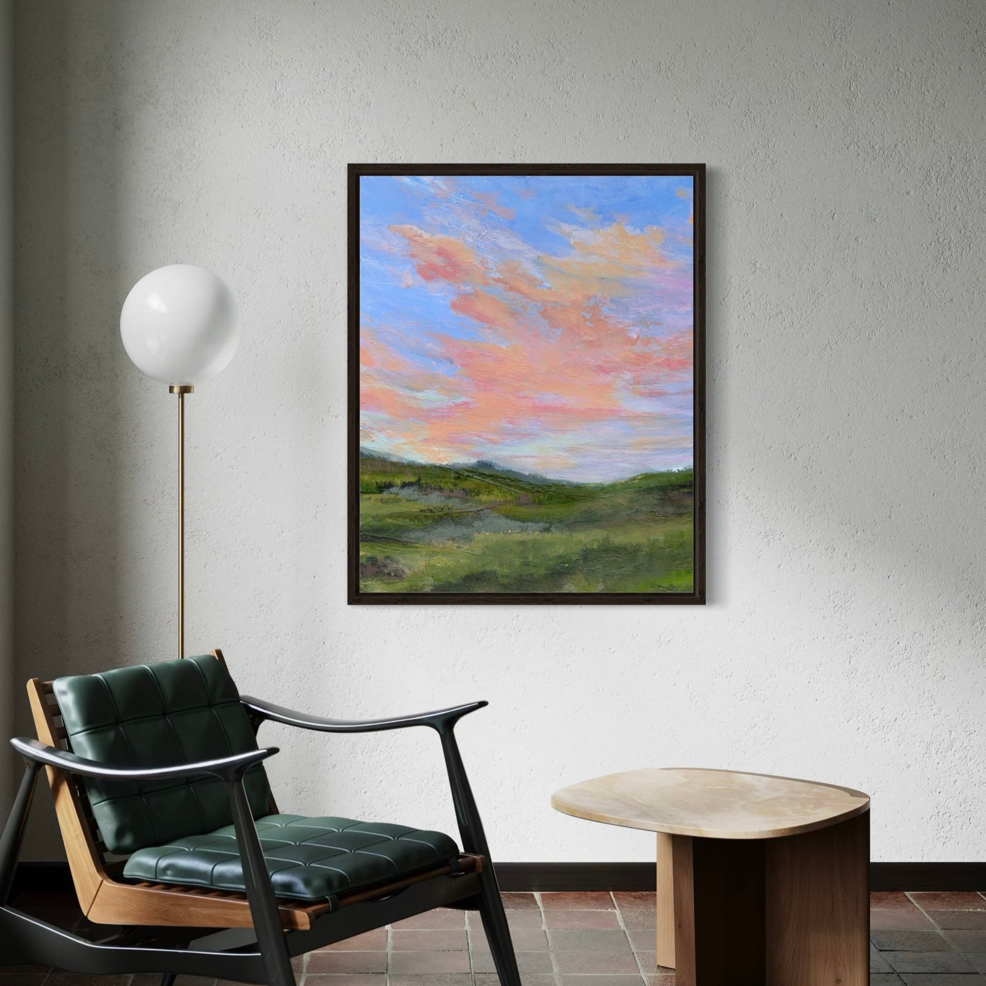 Framed landscape painting on a wall above a chair and table.