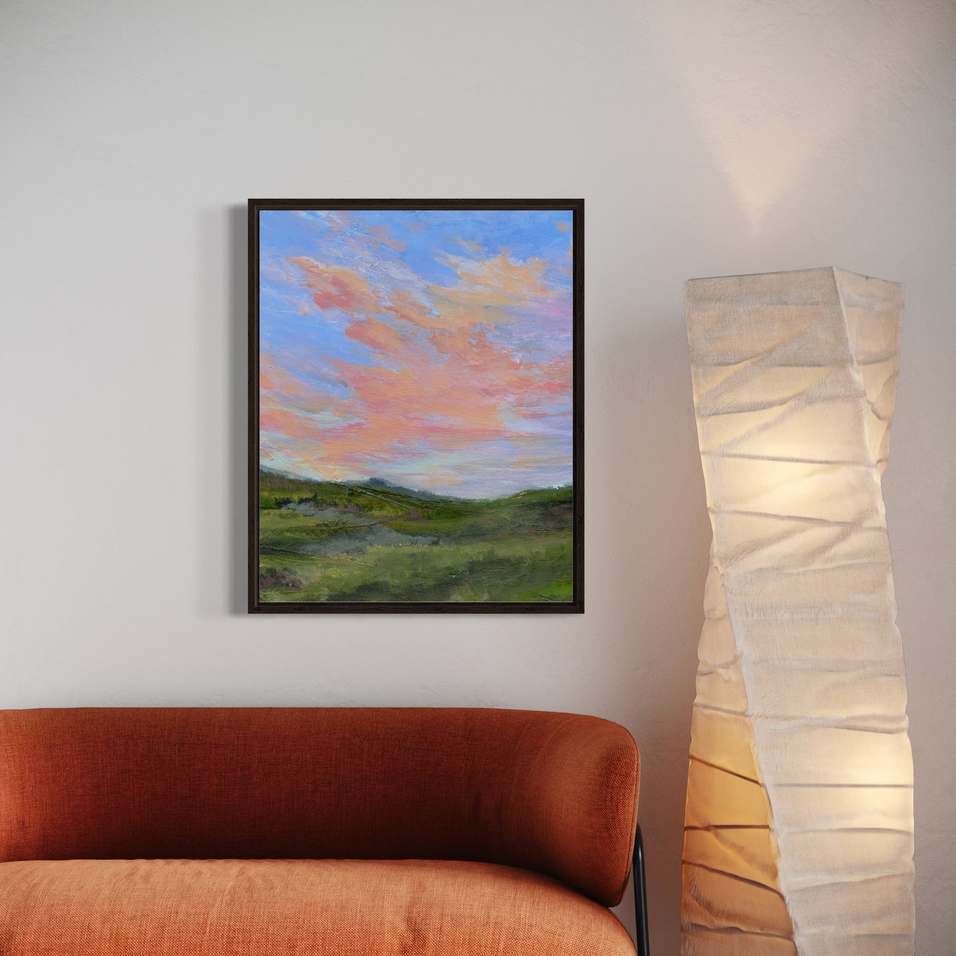 Framed artwork of a landscape with a red sofa and paper lamp in a room.