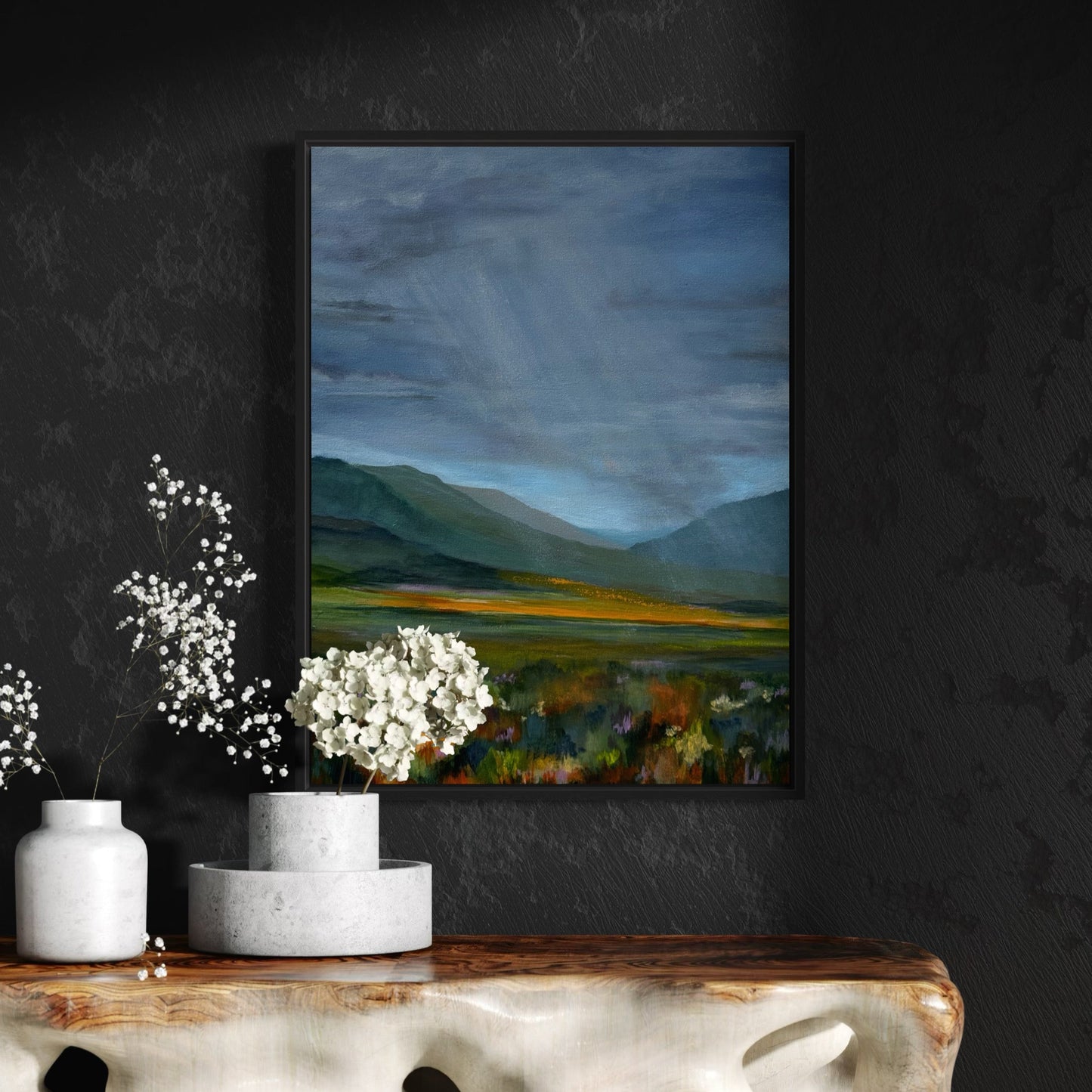 Framed landscape painting on a dark wall with decorative vases and flowers below.