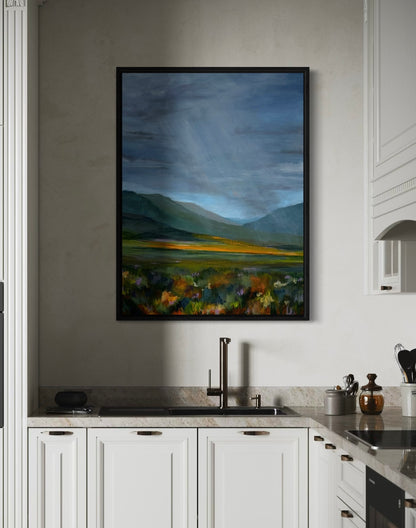 Framed landscape painting above a kitchen sink with white cabinets and modern fixtures.